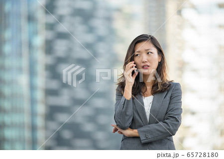 Japanese businesswoman worried look while on voice call, using smartphone, outdoors Japanese businesswoman worried look while on voice call, using smartphone, outdoors 65728180