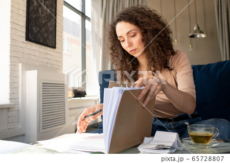 Young serious brunette businesswoman with wavy hair opening journal of expenses 65728807