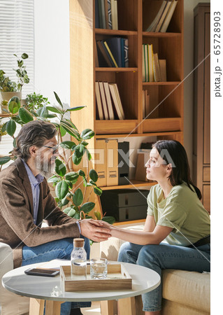 Senior professional counselor with beard holding hands of young female patient Senior professional counselor with beard holding hands of young female patient 65728903