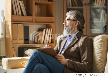 Serious aged professional with grey hair and beard sitting on couch in office Serious aged professional with grey hair and beard sitting on couch in office 65728908