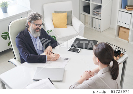 Contemporary employer in formalwear making notes in resumer of new applicant 65728974