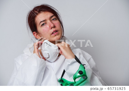 Doctor is taking off PPE - costume, gloves and respirator mask. 65731925