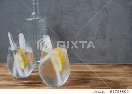 Water with lemon. Refreshing. In transparent glasses, with long ice sticks. Concrete and wood. Water with lemon. Refreshing. In transparent glasses, with long ice sticks. Concrete and wood. 65733309