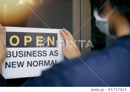 Reopening for business adapt to new normal in the novel Coronavirus COVID-19 pandemic. Rear view of business owner wearing medical mask placing open sign OPEN BUSINESS AS NEW NORMAL on front door. Reopening for business adapt to new normal in the novel Coronavirus COVID-19 pandemic. Rear view of business owner wearing medical mask placing open sign OPEN BUSINESS AS NEW NORMAL on front door. 65737024