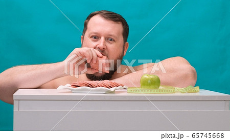 bearded fat man chooses between a sausage or a green apple on a green screen. Man chooses junk food 65745668