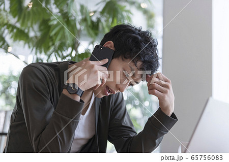 スマートフォンで通話をしながら顔をしかめる男性 65756083