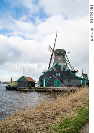 広がる曇り空の下 オランダアムステルダム郊外の川沿いに並ぶ風車と様々な色の家並み 広がる曇り空の下 オランダアムステルダム郊外の川沿いに並ぶ風車と様々な色の家並み 65759961