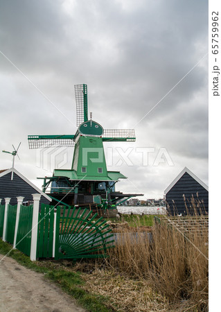 広がる曇り空の下 オランダアムステルダム郊外の川沿いに並ぶ風車と様々な色の家並み 広がる曇り空の下 オランダアムステルダム郊外の川沿いに並ぶ風車と様々な色の家並み 65759962