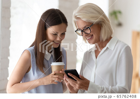 Smiling female colleagues browse smartphone at office coffee break Smiling female colleagues browse smartphone at office coffee break 65762408