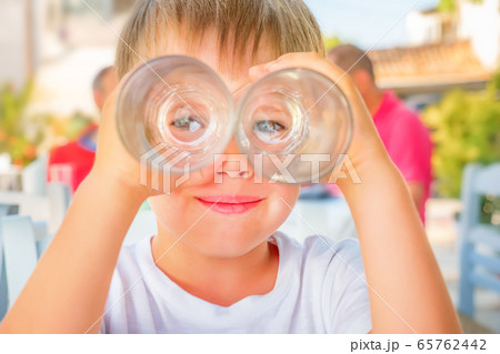 Funny kid looking through two drink glasses as if Funny kid looking through two drink glasses as if 65762442