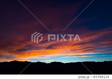 A stunning sunset or sunrise scene of silhouette mountain peaks and purple ridges with the twilight background, the blue sky and the pink-yellow skyline A stunning sunset or sunrise scene of silhouette mountain peaks and purple ridges with the twilight background, the blue sky and the pink-yellow skyline 65769124