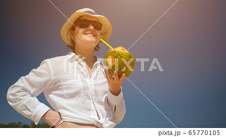 lady stands and drinks coconut with straw against blue sky lady stands and drinks coconut with straw against blue sky 65770105
