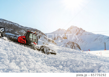 Red modern snowcat ratrack with snowplow snow grooming machine preparing ski slope piste hill at alpine skiing winter resort Ischgl in Austria. Heavy machinery mountain equipment track vehicle 65770292
