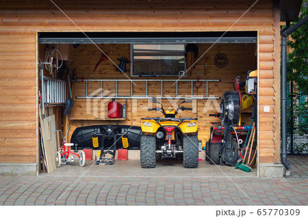 Facade front view open door ATV quad bike motorcycle parking messy garage building with wooden siding at home driveway backyard and lawn path. House warehouse for tools and equipment . Garage sale 65770309