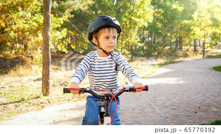 Little toddler boy riding bicycle on path at park Little toddler boy riding bicycle on path at park 65770392