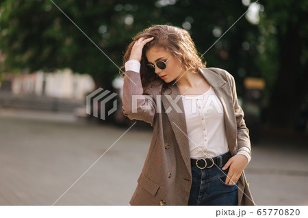 Portrait of attractive woman with curly hair in sunglasses outdoors. Happy young woman walking in the city Portrait of attractive woman with curly hair in sunglasses outdoors. Happy young woman walking in the city 65770820
