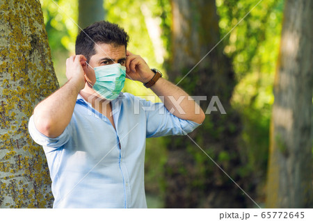 Young man standing in the park removing protective face mask celebrating victory over coronavirus 65772645