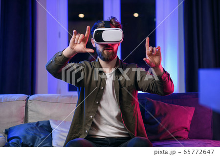 Slow motion of likable cheerful positive man with beard which working on the imaginary touchscreen in augmented reality goggles Slow motion of likable cheerful positive man with beard which working on the imaginary touchscreen in augmented reality goggles 65772647