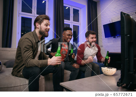 Likable joyful multiracial young guys cheering their favourite football team with screams and hands up during watching sport game on tv Likable joyful multiracial young guys cheering their favourite football team with screams and hands up during watching sport game on tv 65772671