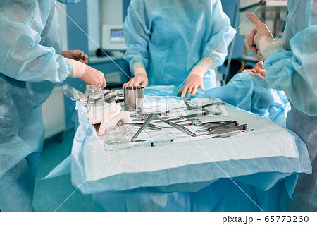 Sterile instruments on the operating table, a team of doctors lays out the instruments for the operation. many hands are brewing in sterile gloves. 65773260