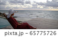 Beautiful young woman sits by the ocean taking in sunset while on vacation 65775726