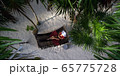 Woman rests in loose red summer dress and hat hanging in hammock surrounded by palm trees at sunset 65775728