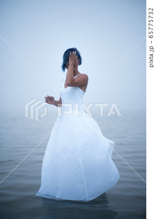 Cute shy girl covers her face in white dress and blue hair looks as if she is drifting by water Cute shy girl covers her face in white dress and blue hair looks as if she is drifting by water 65775732