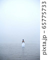 Woman in white dress and blue hair looks as if she is drifting by water surrounded by mist and fog  65775733