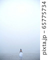 Woman in white dress and blue hair looks as if she is drifting by water surrounded by mist and fog  65775734