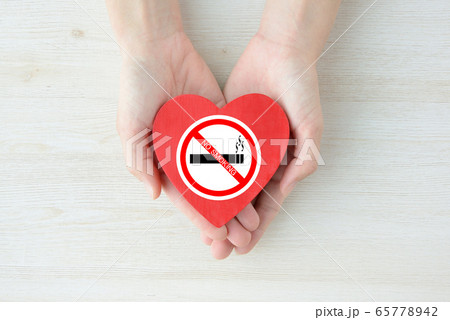 禁煙ステッカーを貼ったハートのオブジェを持つ人物の手 65778942