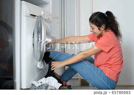 Girl kicks dirty laundry in the washing machine. A 65780983