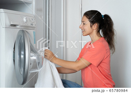 A girl loads dirty laundry into a washing machine A girl loads dirty laundry into a washing machine 65780984