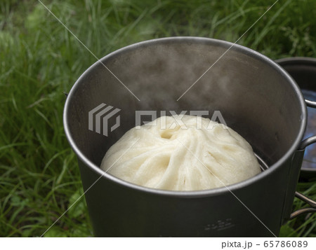 山でコッヘルを使ってアウトドア調理する湯気立つ蒸したての豚まん 65786089