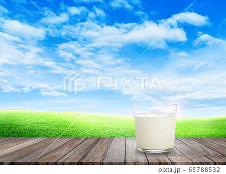 White milk in glass on wooden table with green grass field and little hill in background. White milk in glass on wooden table with green grass field and little hill in background. 65788532