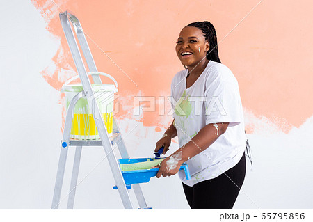 Afro woman painting the walls of new home. Renovation, repair and redecoration concept. Afro woman painting the walls of new home. Renovation, repair and redecoration concept. 65795856