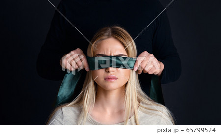 Abuzer concept. Man in black tying female eyes with green ribbon 65799524