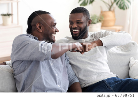 Father-Son Friendship. Black Millennial Guy Bumping Fists With Senior Dad At Home 65799751