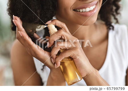 Split Ends Treatment. Smiling Black Woman Spraying Essential Oil On Curly Hair 65799799