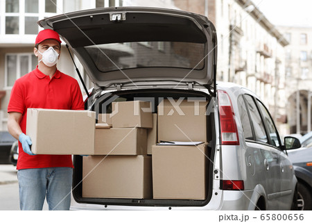 Many orders, a lot of deliveries concept. Courier holds big parcel near the car 65800656