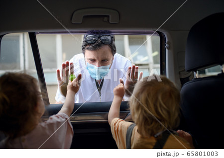 Doctor coming to see family in isolation, car window glass separating them. 65801003