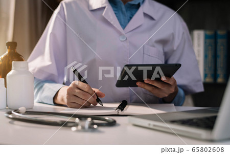 Doctor working on laptop computer, writing prescription clipboard with record information paper folders on desk in clinic, Healthcare and medical concept. Doctor working on laptop computer, writing prescription clipboard with record information paper folders on desk in clinic, Healthcare and medical concept. 65802608