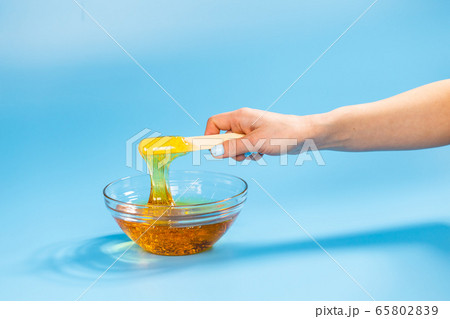 Female hands take out sugar paste for sugaring with a wooden spatula on blue background. Epilation and hair removal concept. Female hands take out sugar paste for sugaring with a wooden spatula on blue background. Epilation and hair removal concept. 65802839
