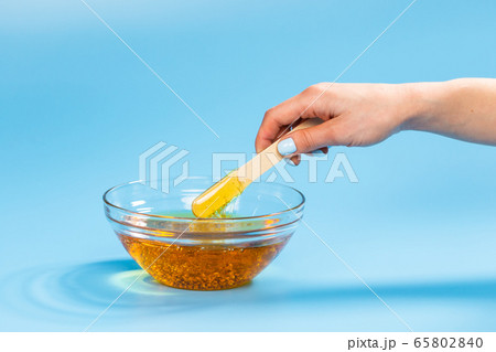 Depilation and beauty concept - sugar paste or honey wax for hair removing spatula with wooden framing sticks on a bright blue background Depilation and beauty concept - sugar paste or honey wax for hair removing spatula with wooden framing sticks on a bright blue background 65802840