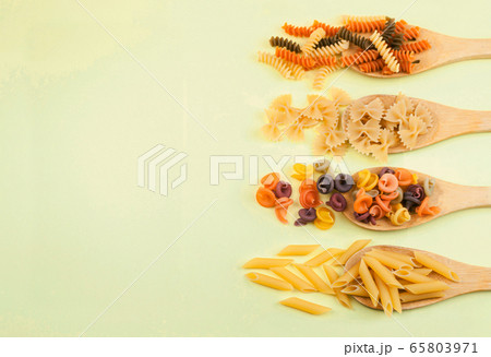 various pasta of Italian cuisine. Farfalle, penne rigate, fusilli on wooden spoons on a yellow background. Top view, copy space. various pasta of Italian cuisine. Farfalle, penne rigate, fusilli on wooden spoons on a yellow background. Top view, copy space. 65803971