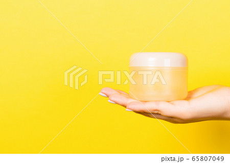 Female hand holding cosmetics jar at yellow Female hand holding cosmetics jar at yellow 65807049