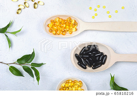 Black pill, yellow pill and wooden spoon on light background 65810216