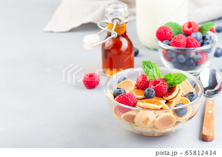 Tiny cereal pancakes served with maple syrup 65812434