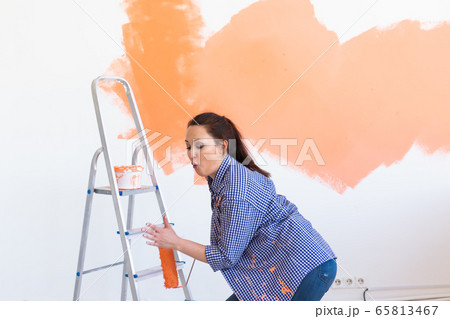 Dancing funny woman painting interior wall of home. Renovation, repair and redecoration concept. 65813467