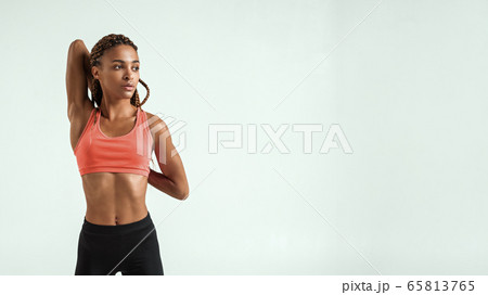 Warming up. Beautiful young african woman in sportswear stretching her arms while standing against grey background Warming up. Beautiful young african woman in sportswear stretching her arms while standing against grey background 65813765