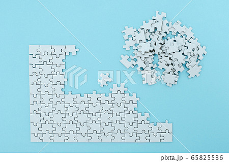 ステイホームで集中力アップの為の水色背景に置かれた作業途中の無地のジグソーパズルの写真素材